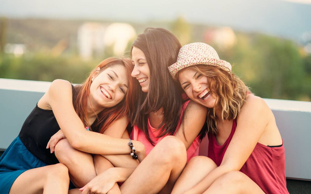 Three friends smiling and laughing as they lean against each other.