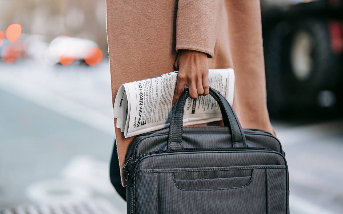Someone holding a newspaper and briefcase handle in one hand.