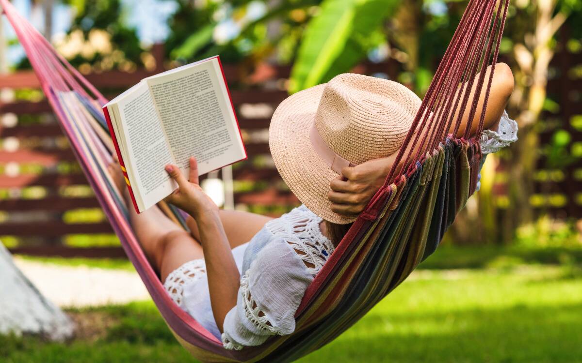 A woman lounging in a hammock, reading.