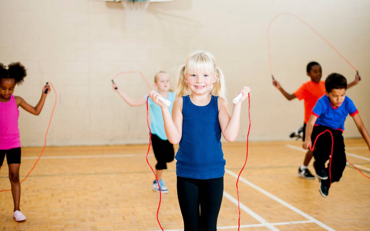 A kid standing in a gym holding a jump rope.