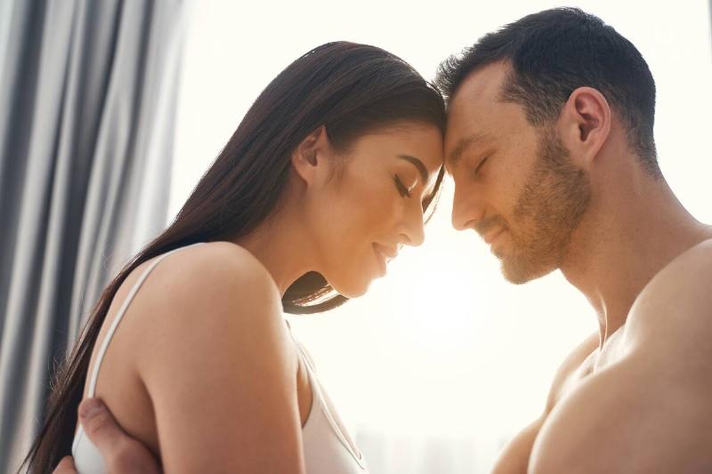 couple seated face to face touching foreheads with sun in background