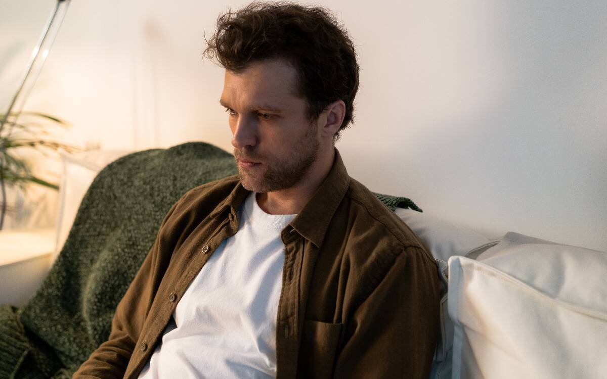 A man sitting on a couch, staring forward, looking sad.