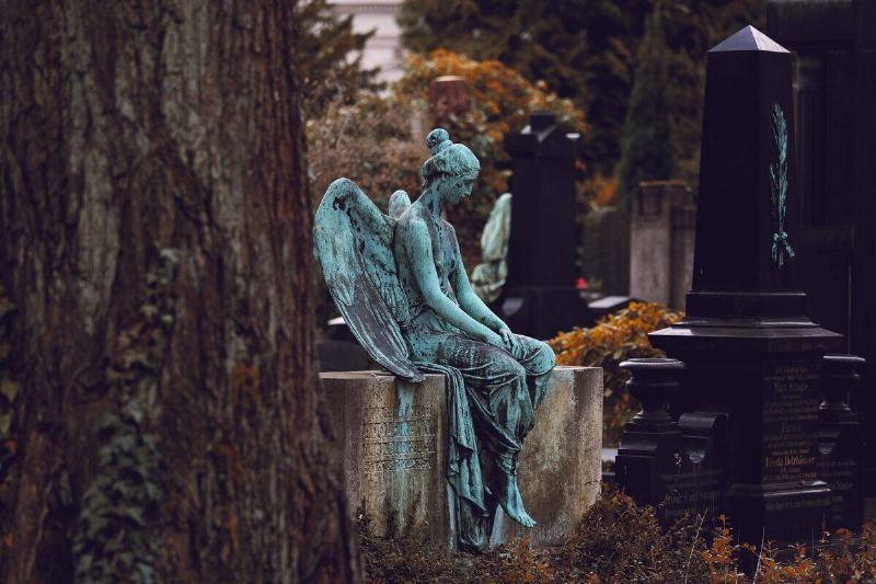 stone angel sitting on perch in cemetery