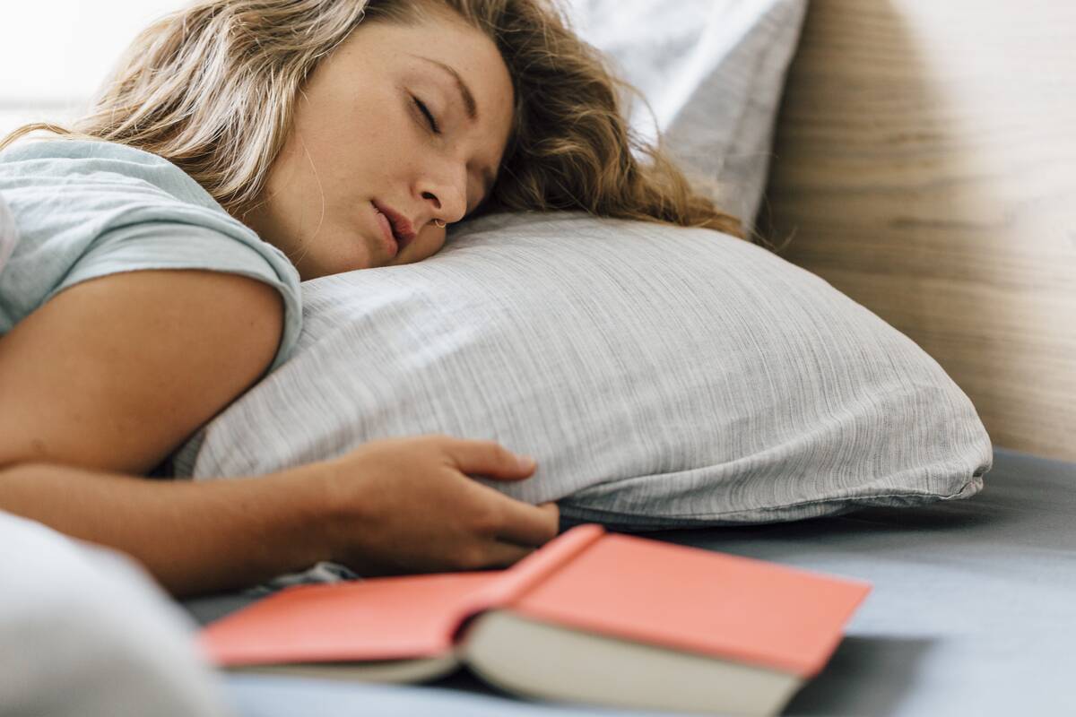 A woman asleep with an open book placed page-down next to her.