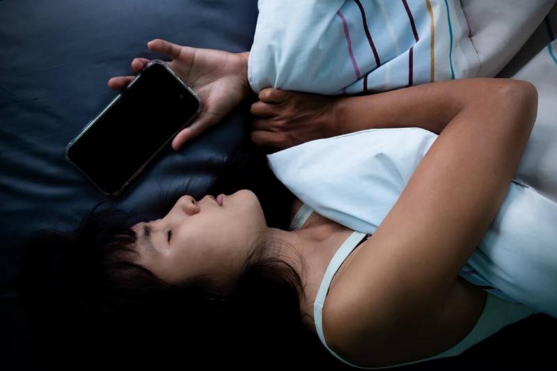 A woman asleep in bed with her phone next to her head, loosely still in her hand.