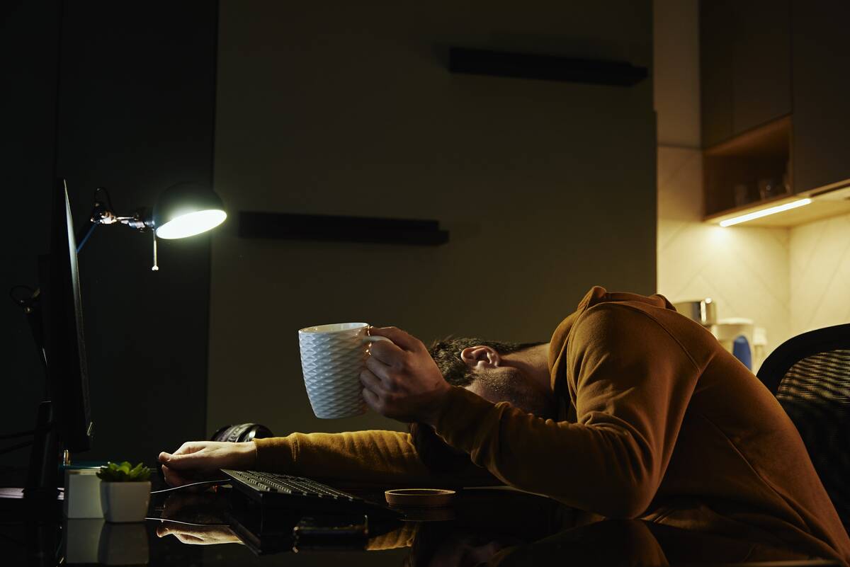 Man asleep at desk with cup of coffeee in his hand.