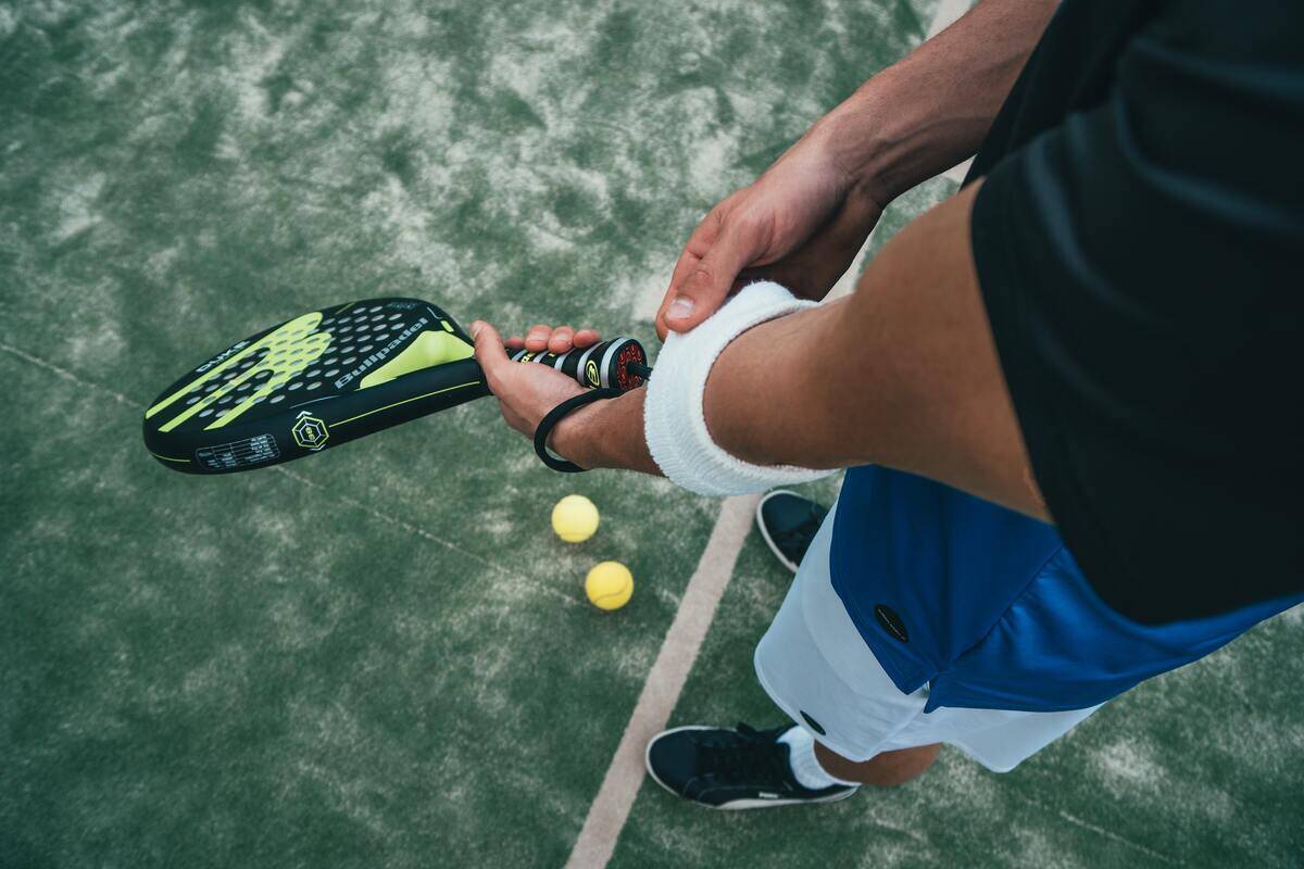 A man adjusting an armband as he holds a tennis racket.