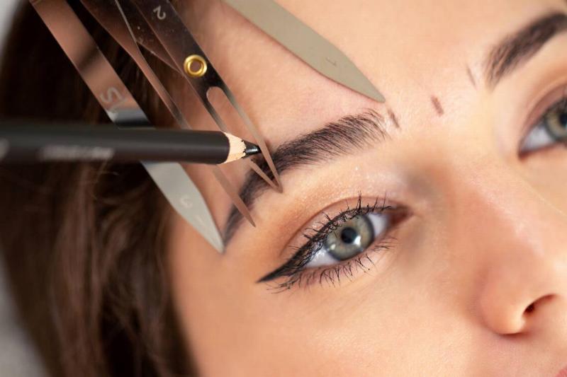 Someone measuring another person's eyebrow to draw them on correctly.