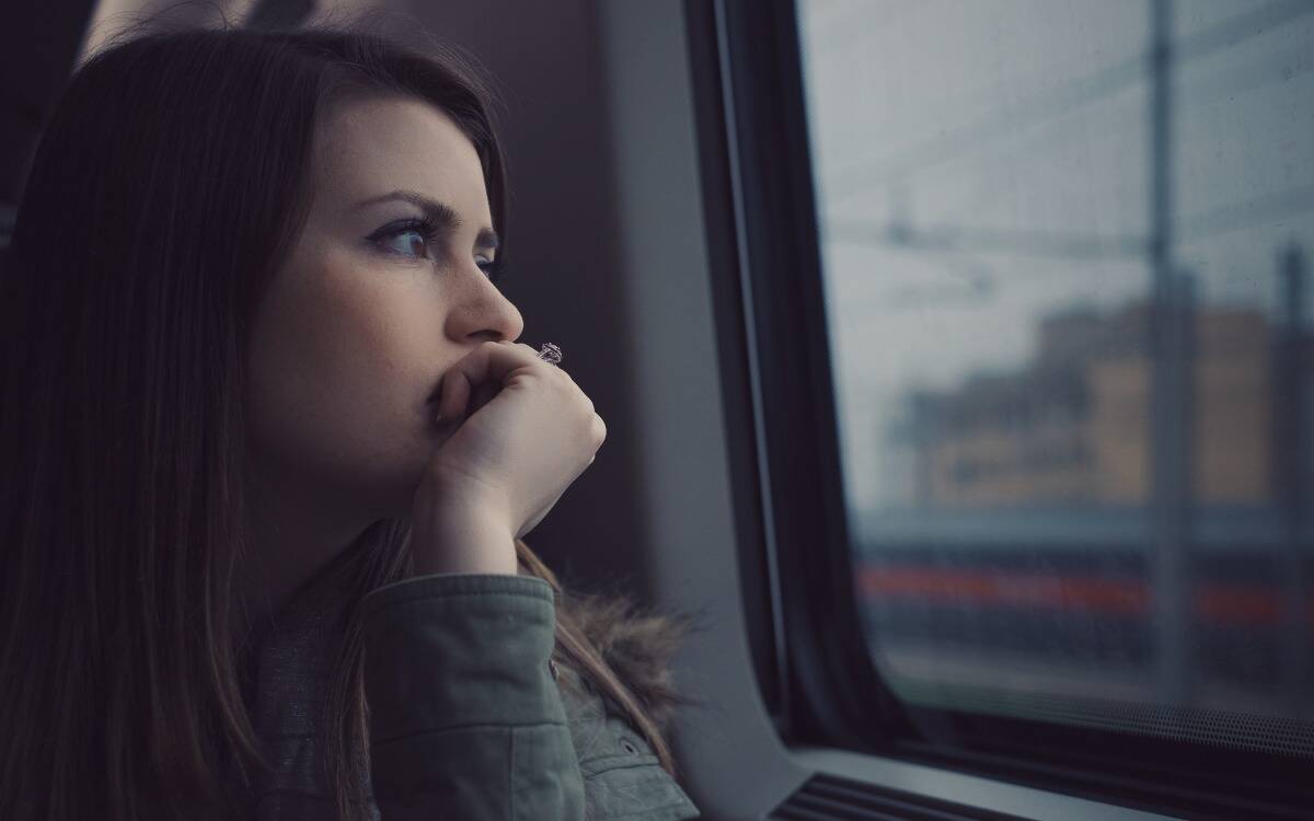 A woman looking sorrowfully out a window, her chin in her hand.