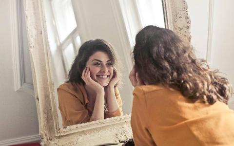 A woman smiling as she looks in the mirror.