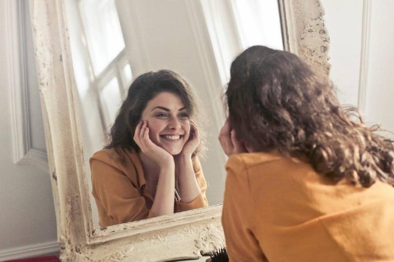 A woman smiling as she looks in the mirror.
