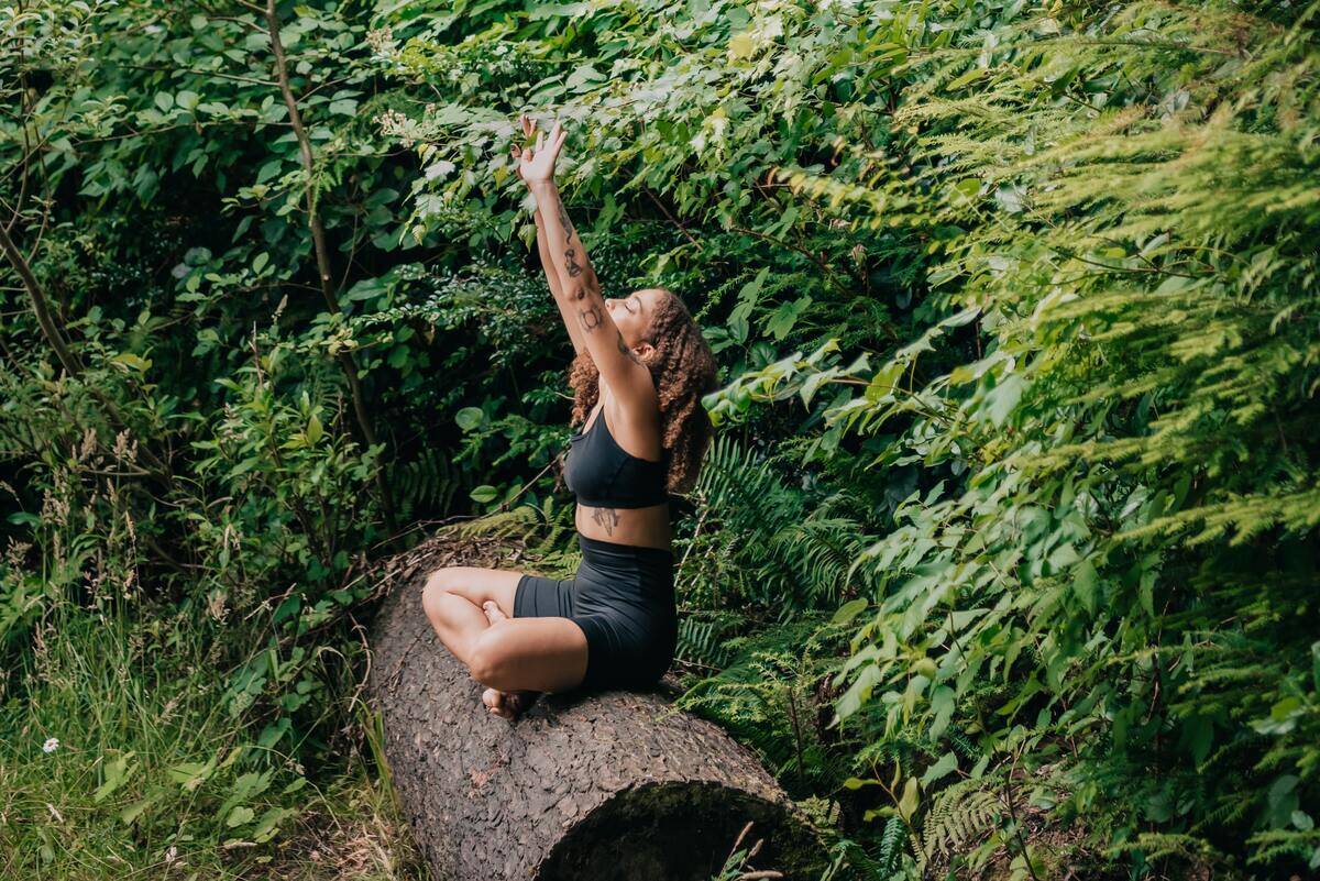 A woman mediating atop a tree trunk in the forest.