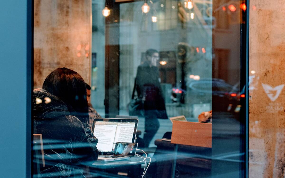 Someone working at their laptop in a cafe, seen through a window.
