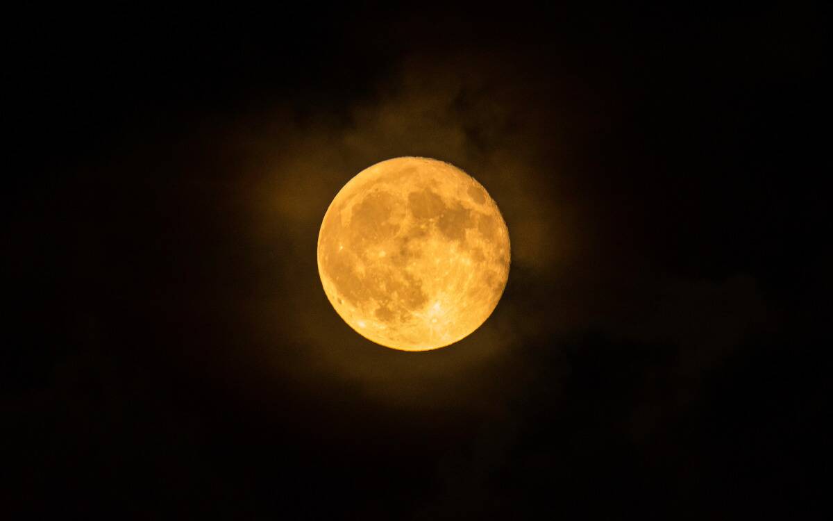 A golden moon in a cloudy dark sky.
