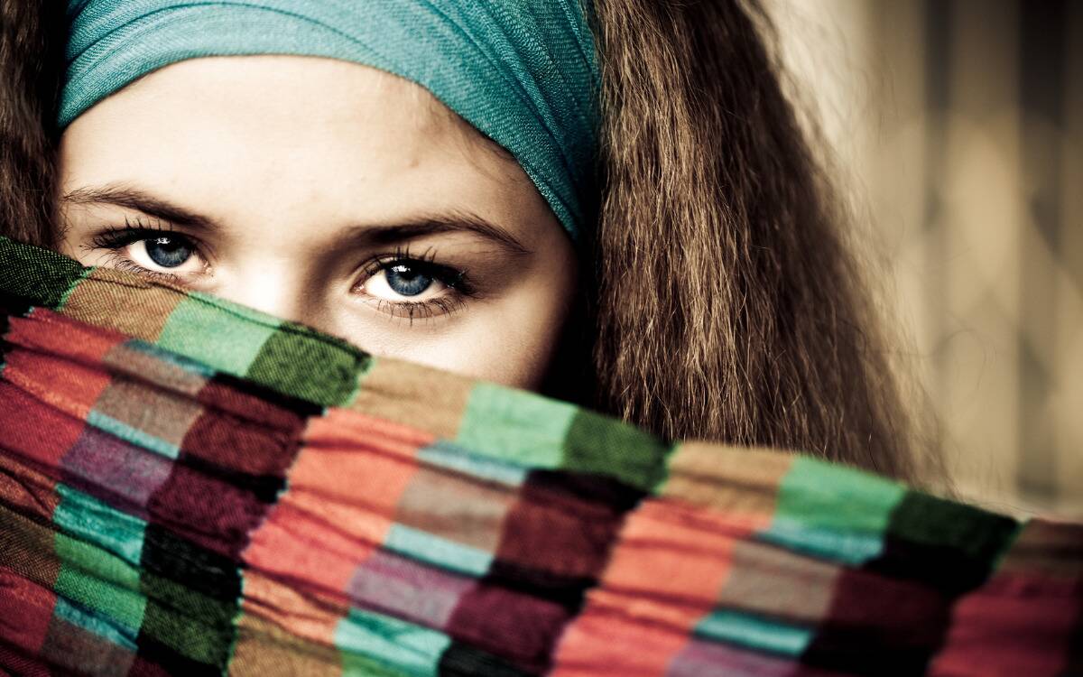 A woman with an intense gaze looking over her scarf that's covering the lower half of her face.