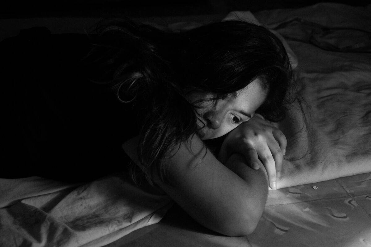 A greyscale image of a woman laying on her stomach in bed, arms folded under her head.