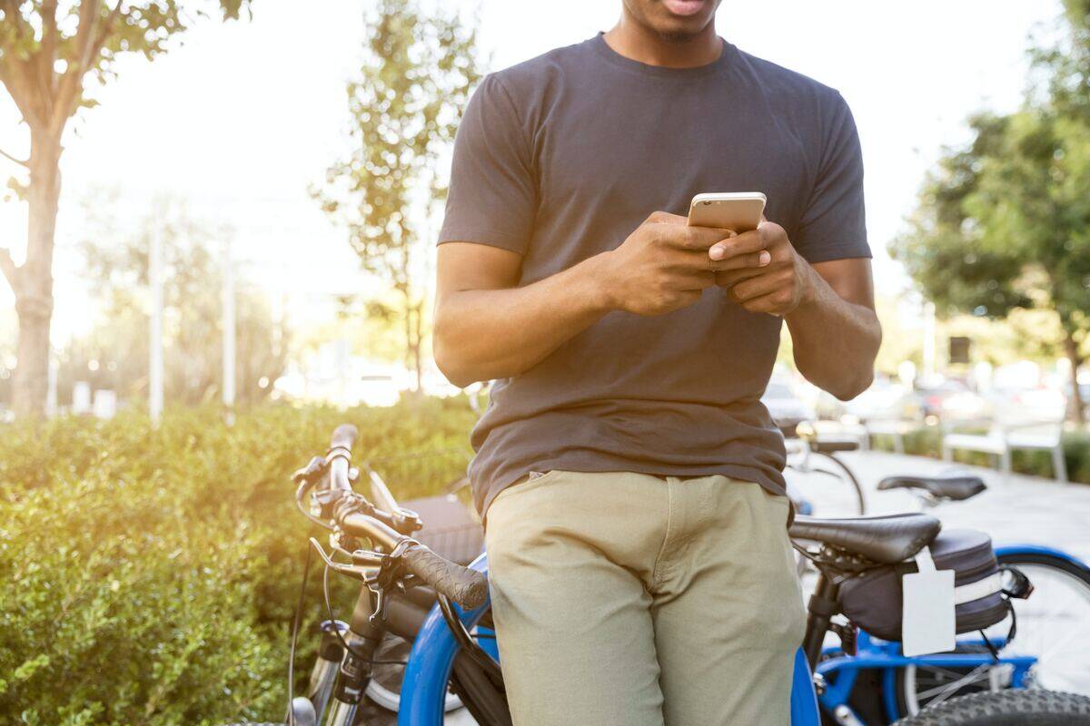 A man checking his phone outside, leaning against a bike rack.