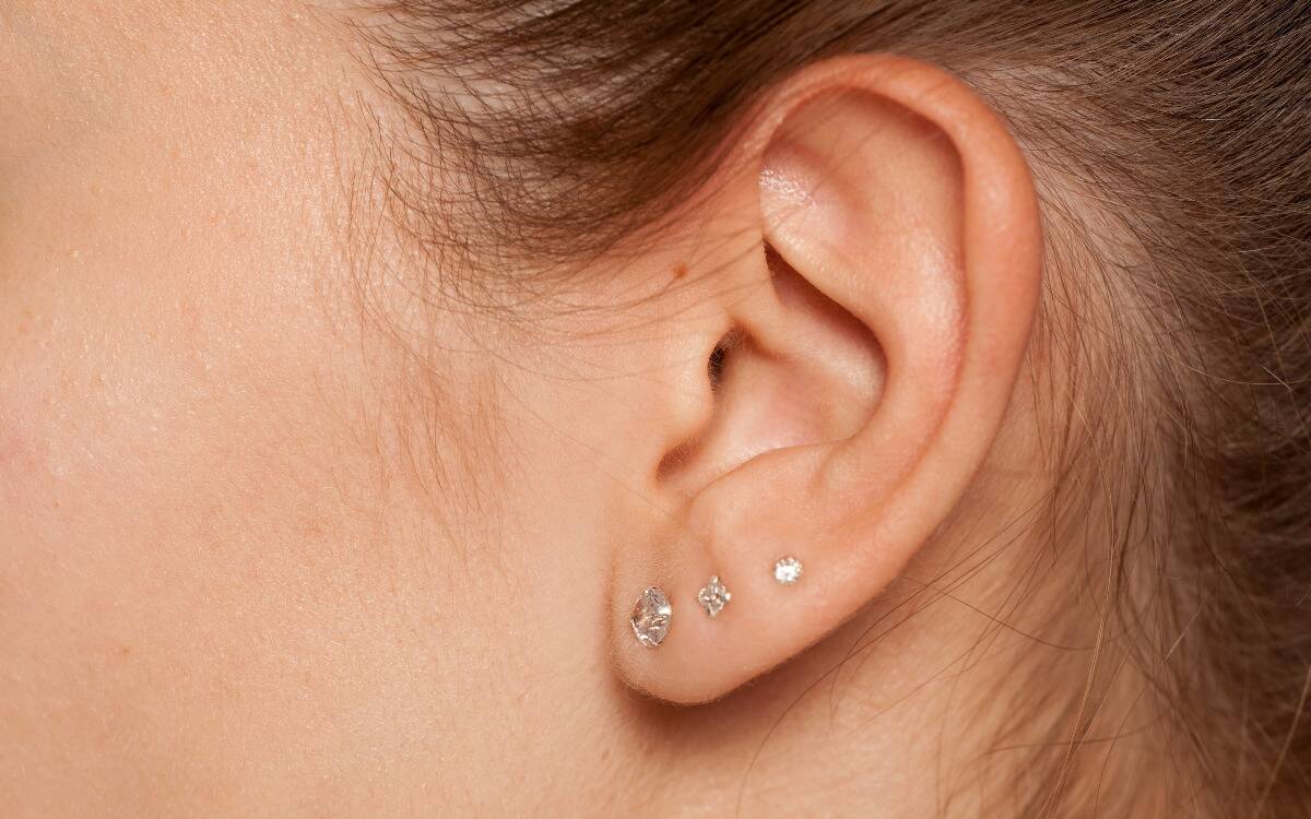 A closeup of a woman's ear, three small diamond earrings in the lobe.