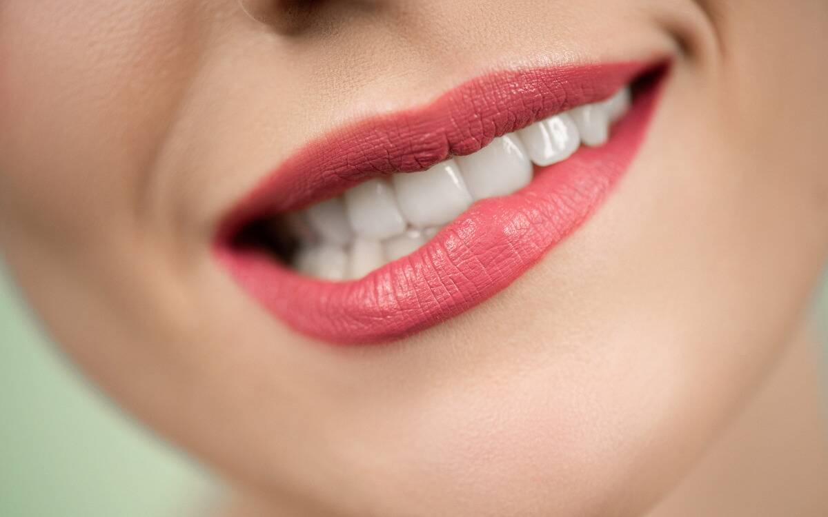 A closeup of a woman's mouth in pink lipstick, biting her bottom lip.