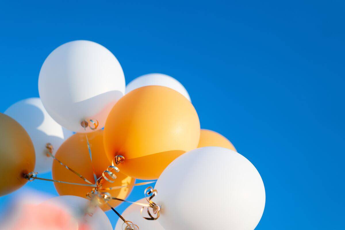 A bundle of yellow and white balloons against a bright blue sky.