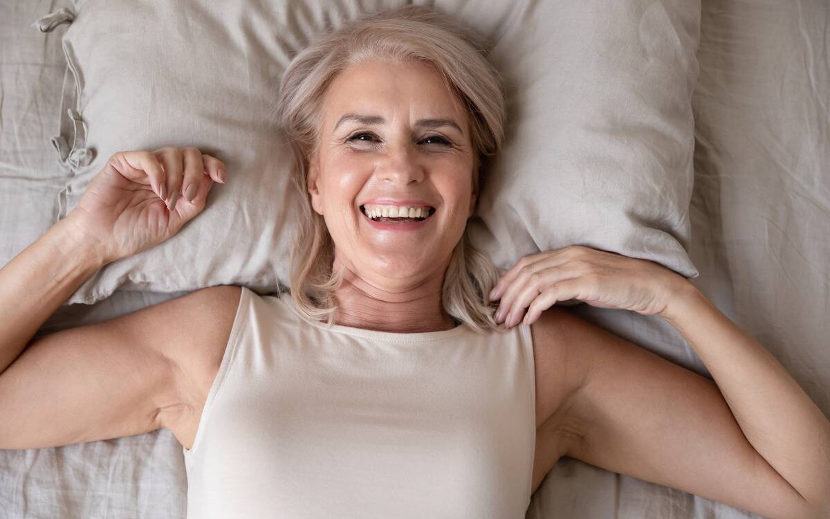 A woman smiling as she lays in bed, hands up by her shoulders