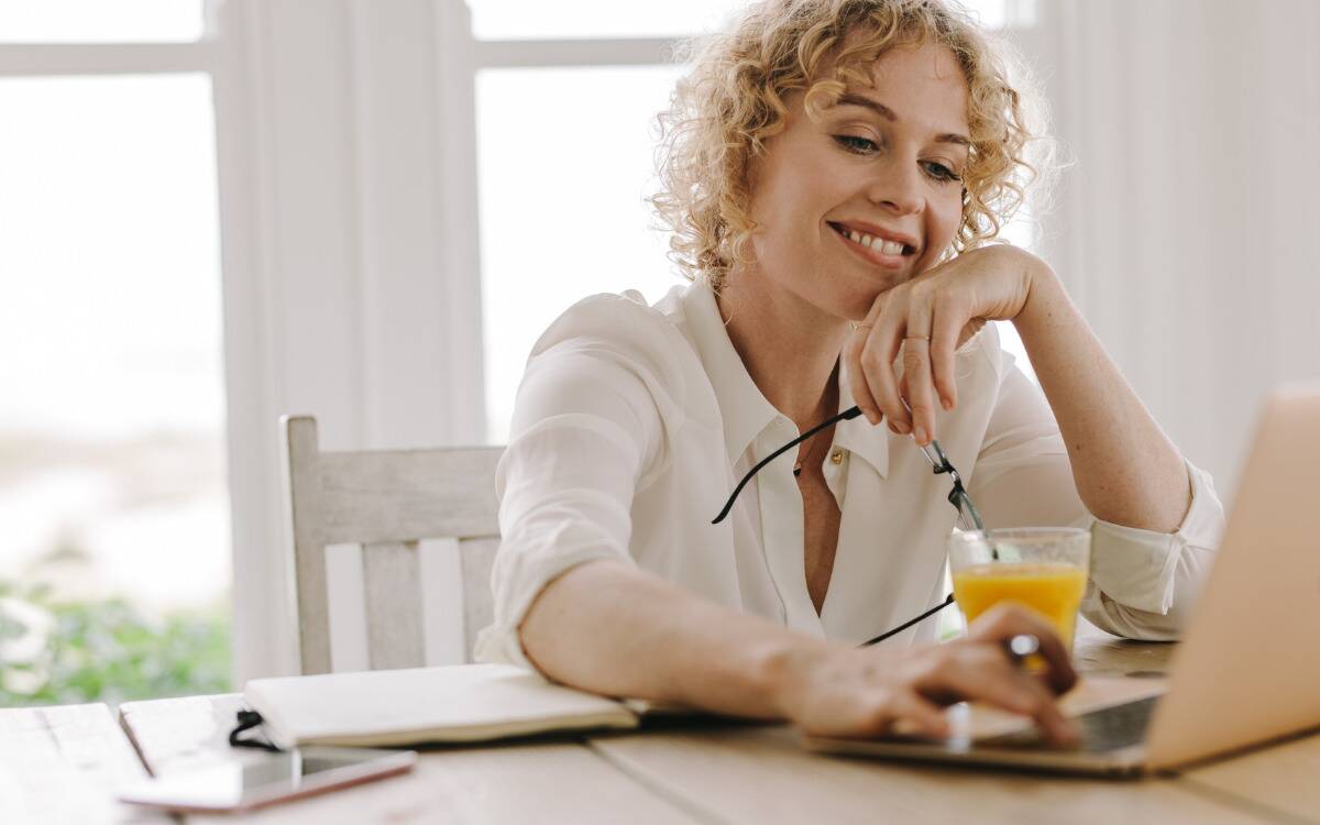 A woman smiling as she does work on her laptop.