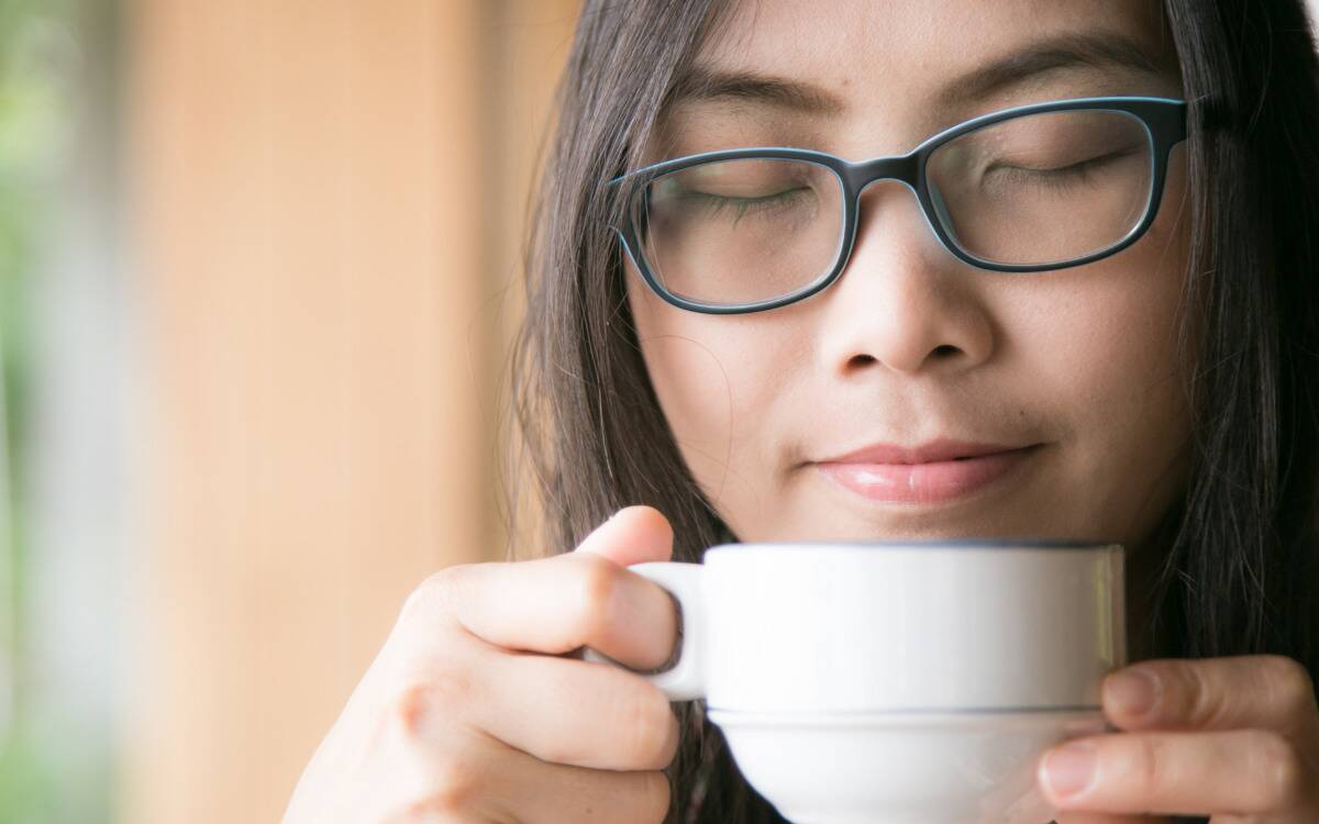 A woman appearing peaceful, a mug being held close to her face.