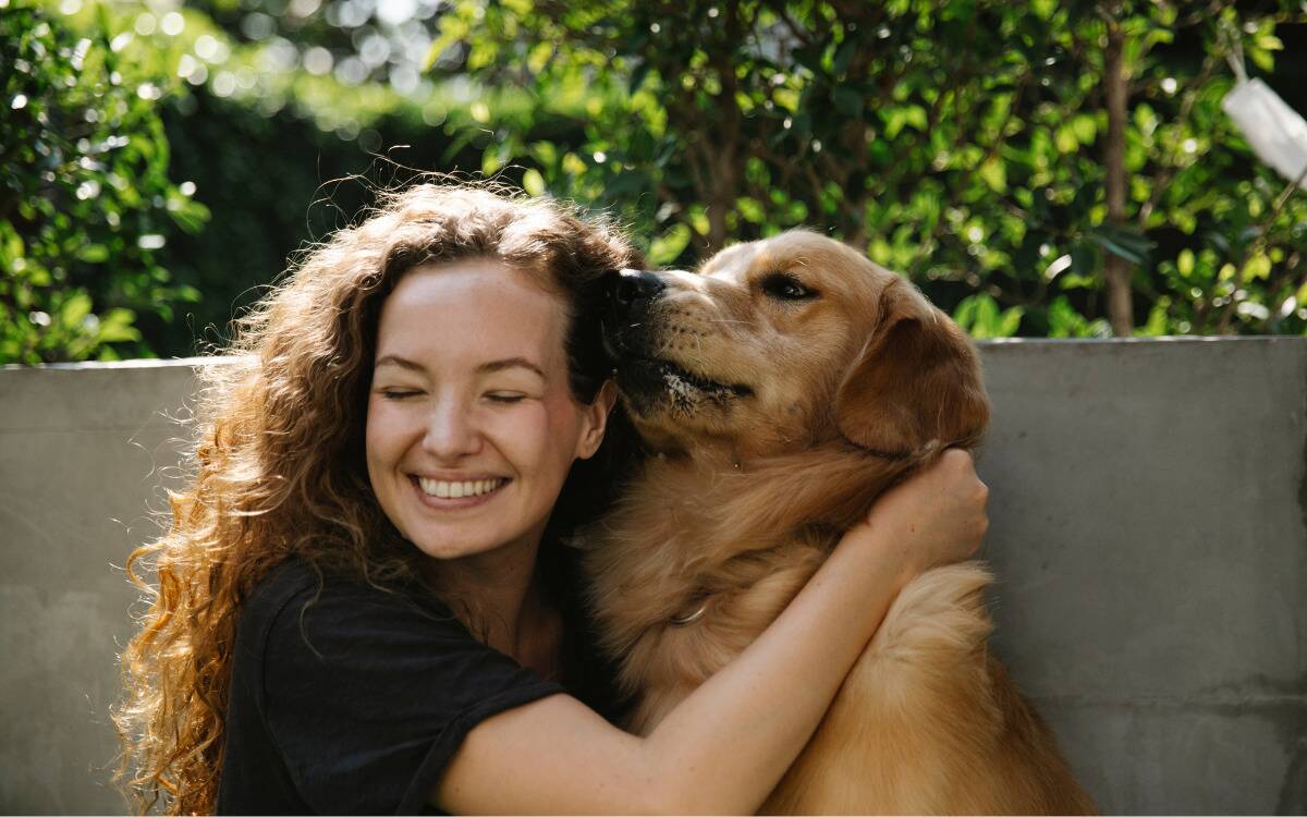 A woman smiling as she cuddles with her dog.