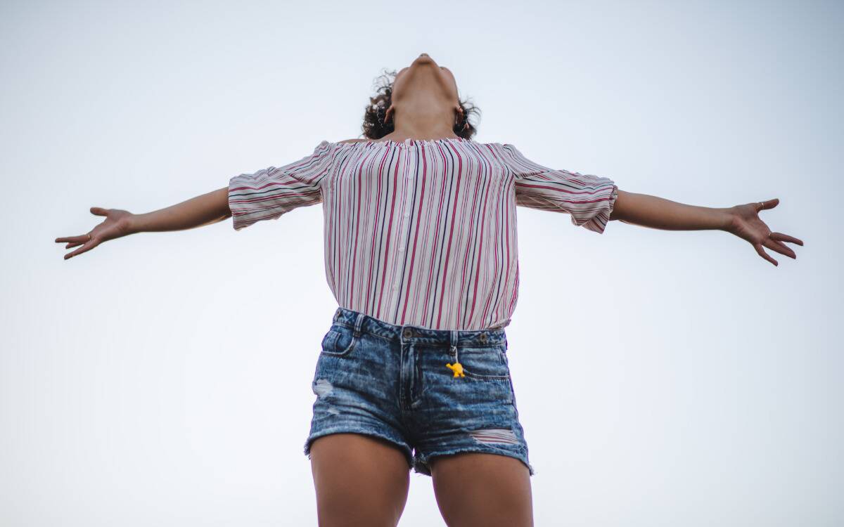 A woman standing outside, looking up, her arms stretched out at her side.