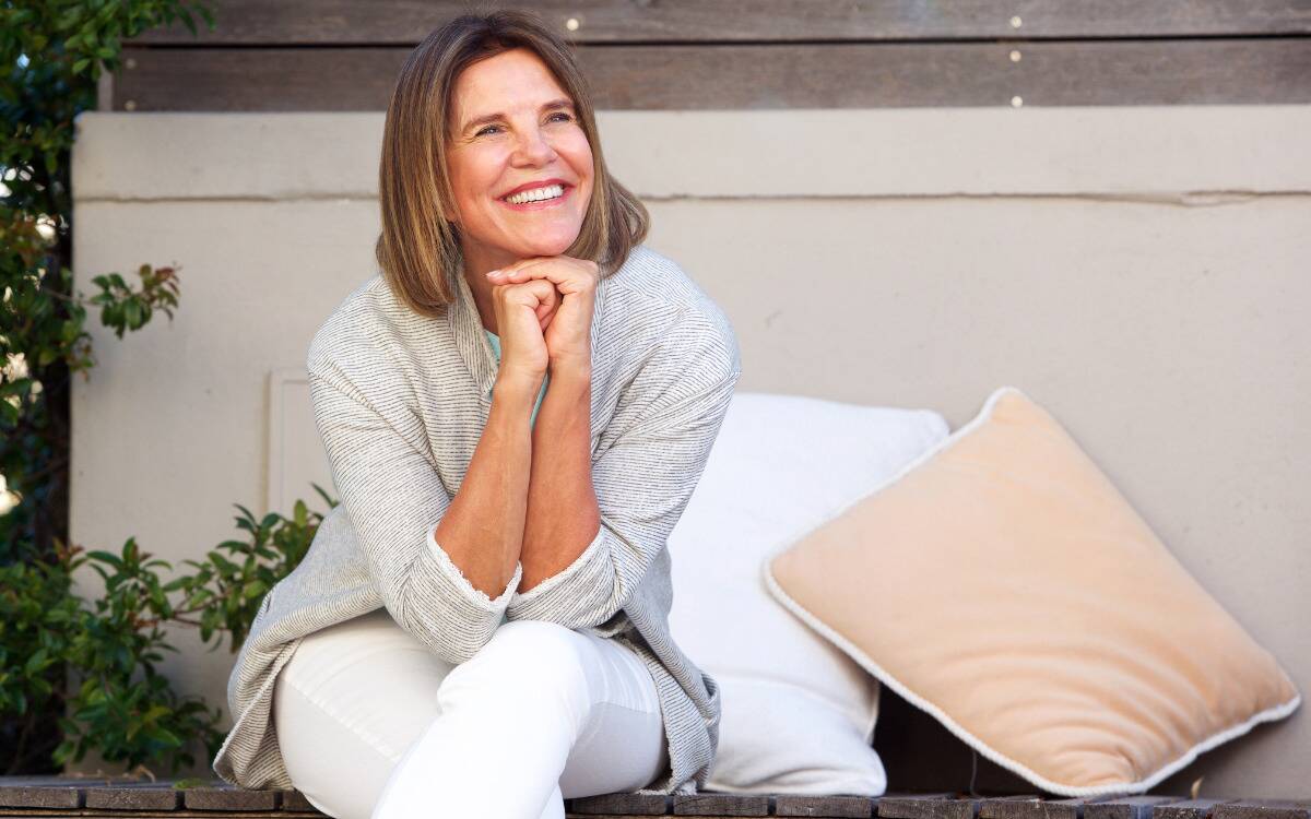 A woman smiling and looking up, chin resting on both hands.