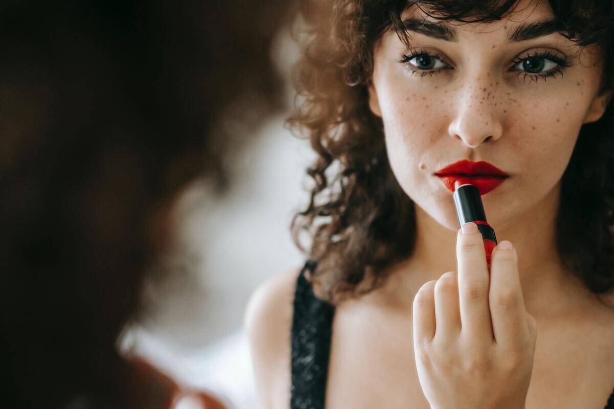 A woman applying bright red lipstick in the mirror.