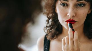 A woman applying bright red lipstick in the mirror.