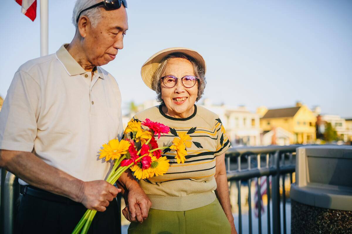 An elderly couple for a walk, the man holding a bouquet of bright flowers.