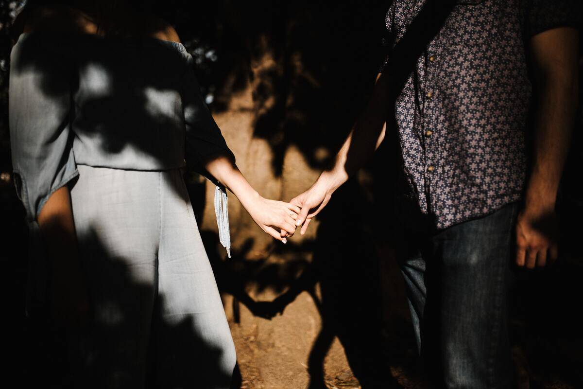 A couple holding hands, the rest of their bodies largely hidden in shadow.