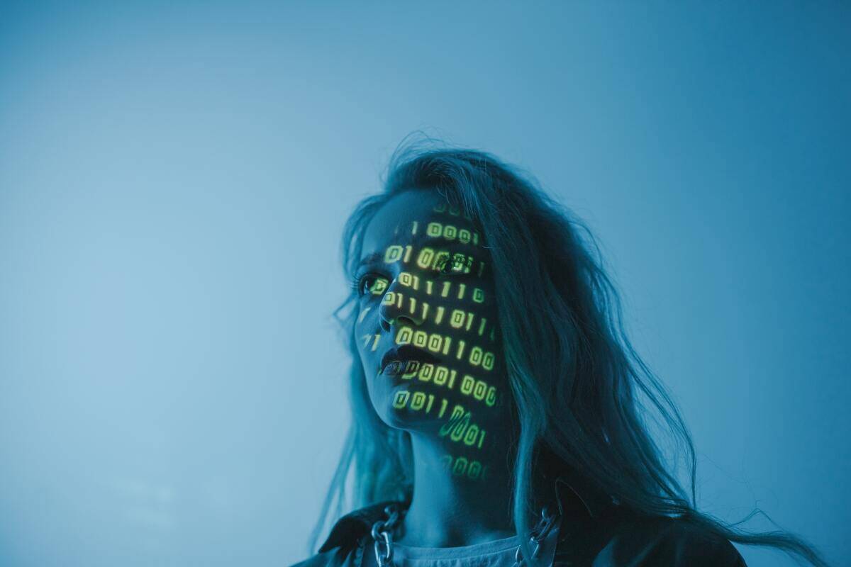 A girl lit in blue with green colored binary code projected onto her face.