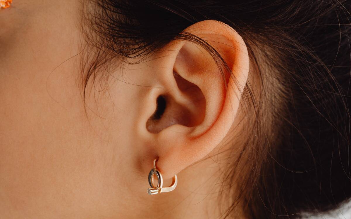 A closeup of someone's ear with a gold, geometric earring in it.