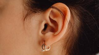 A closeup of someone's ear with a gold, geometric earring in it.