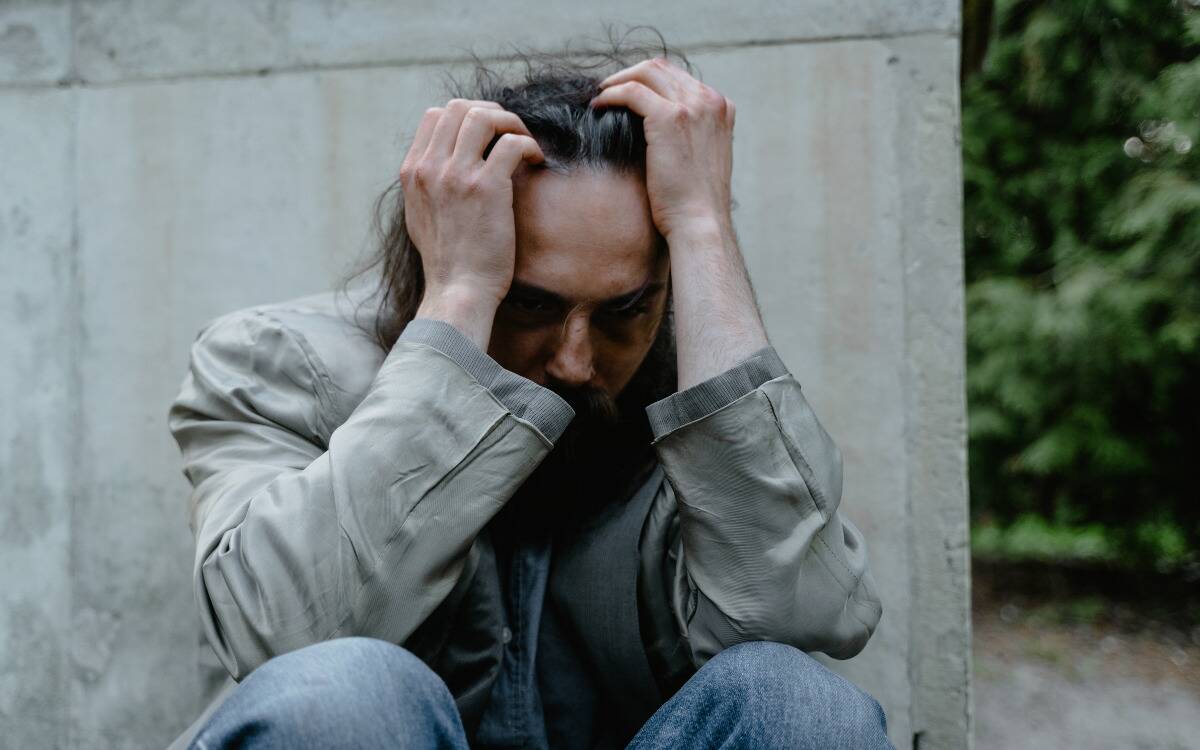 A man sitting on the ground, knees to his chest, hands in his hair.