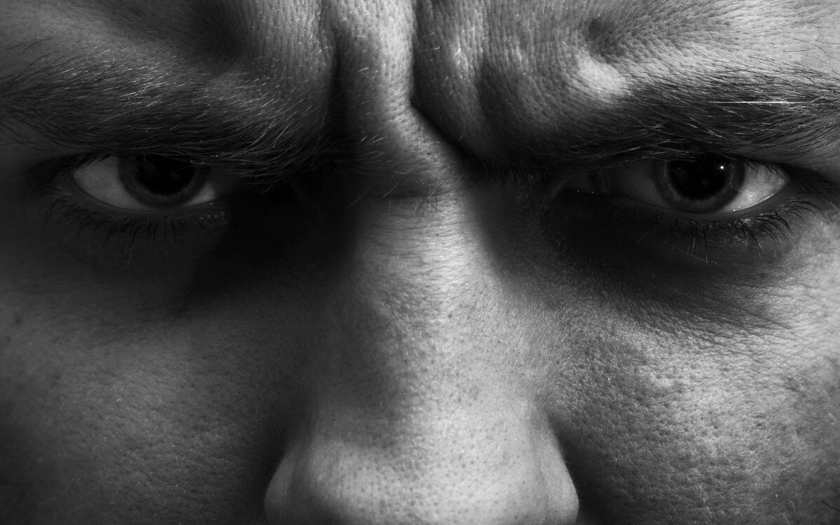 A black and white image of a closeup of a an's angry face. 