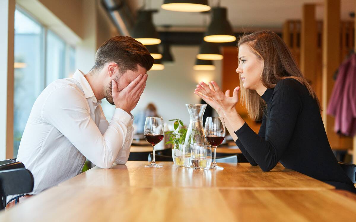 A man and woman arguing while seated at a restaurant.