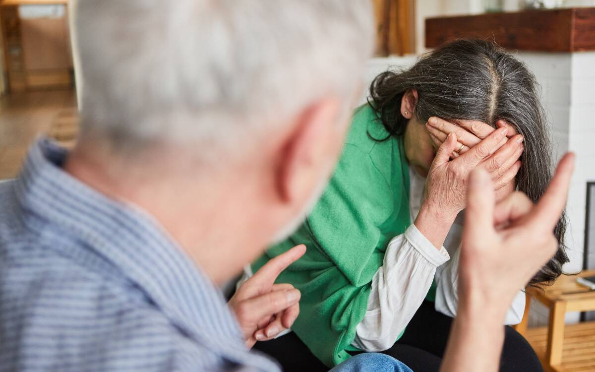 A man openly criticizing his partner, who's hiding her face in shame.