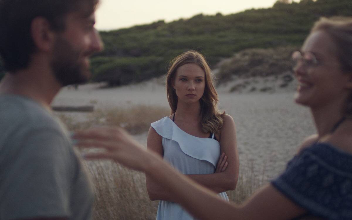 A woman staring with a jealous expression at another woman flirting with a man in front of her.