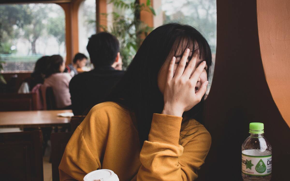 A girl hiding her face behind her hand while at a cafe.