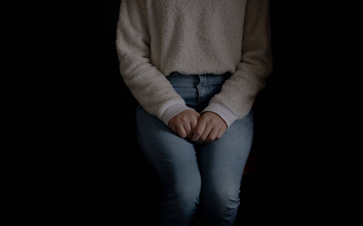 A woman seated in a closed off, shy position in the dark.