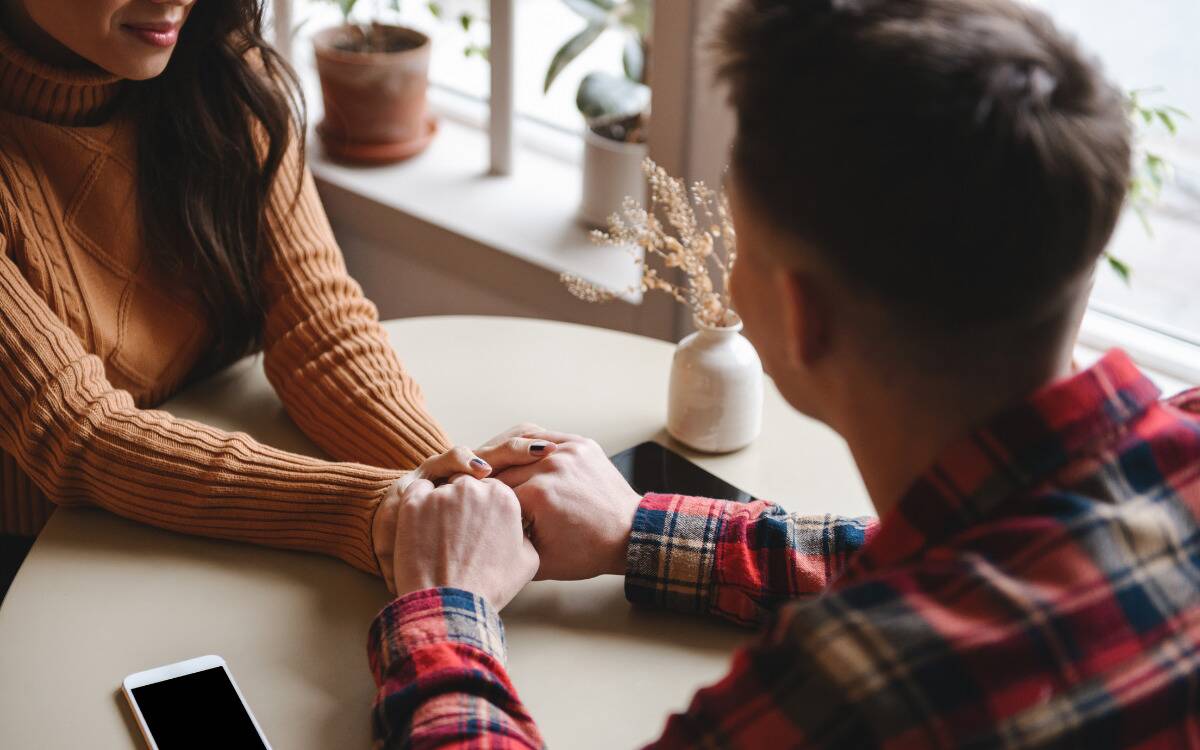 Two people holding hands across a table during a date.