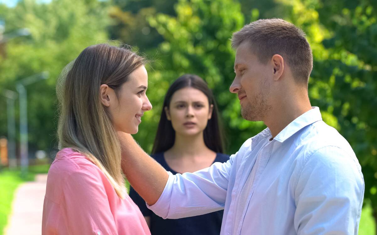 A woman looking jealous and betrayed as a man flirts with someone else in front of her.
