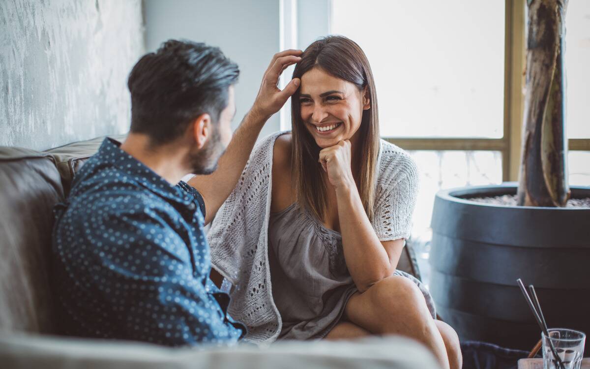 A man caressing a woman's hair as they sit on a couch.