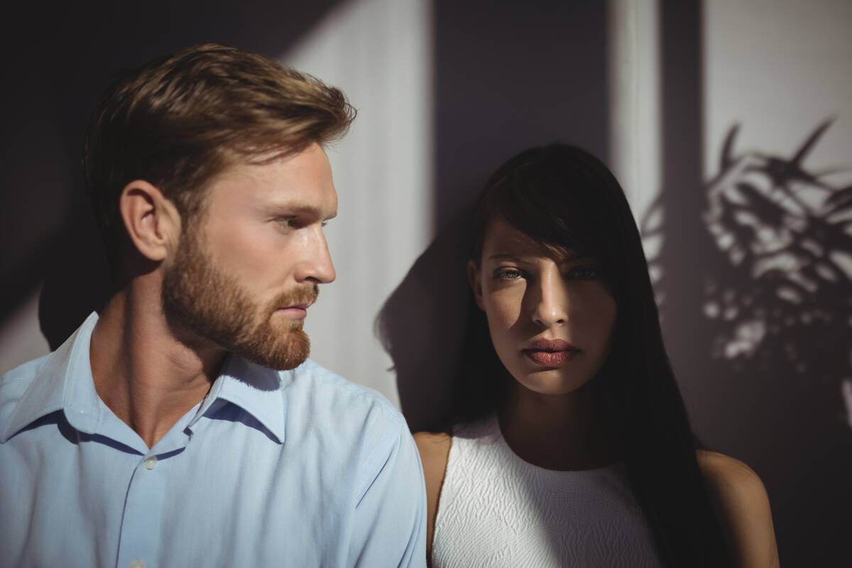 Two confident seeming people lit in shadow against a grey wall.