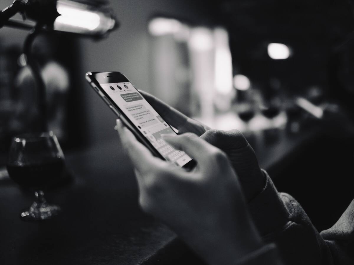 A greyscale closeup image of someone texting on their phone.