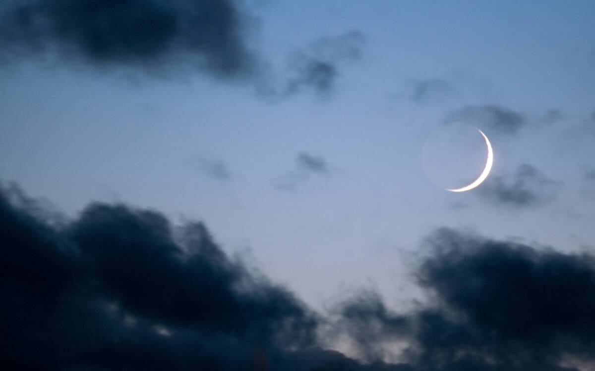 The new moon in a pale blue, but darkly cloudy sky.